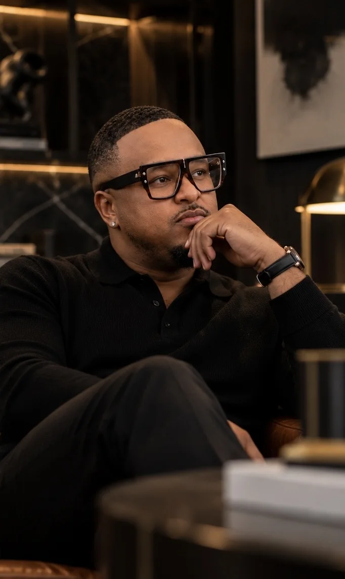 Brennon Jackson, founder of EYEGASMIC, seated in a dark study and looking thoughtfully into the distance.